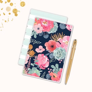 May include: A floral planner with a navy blue background and pink, red, and green flowers. A gold pen rests beside the planner. The planner has a light blue striped cover.