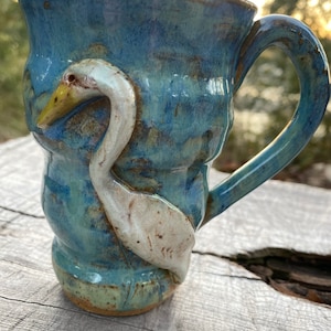 May include: A blue ceramic mug with a white bird sculpted on the side. The mug has a textured, glazed finish.