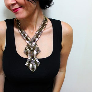 May include: A beaded necklace with a geometric design. The necklace features a combination of gold, white, and black beads, creating a striking pattern. The necklace is worn over a black tank top.