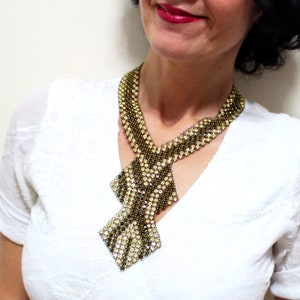 May include: A beaded necklace with a geometric design. The necklace features a combination of gold and silver beads, creating a textured pattern. The necklace has a bib-style design with a diamond-shaped pendant.