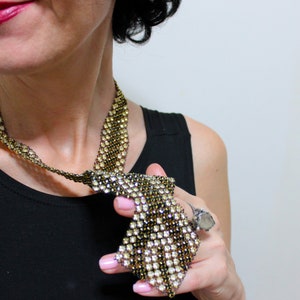 May include: A gold and clear rhinestone necklace with a unique, geometric design. The necklace is made of small, sparkling rhinestones set in a gold-tone metal. The necklace is worn over a black top.