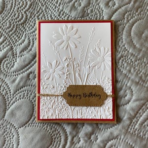 May include: White card with a red border and an embossed design of flowers and leaves. The card has a brown tag with the text "Happy Birthday" on it.