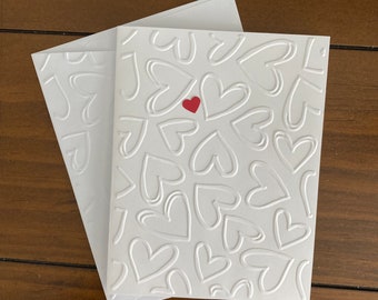 Greeting cards handmade: simple, elegant Valentine. Bright white card stock is embossed with hearts. Red and white.