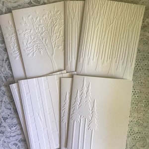 May include: A set of eight blank white greeting cards with embossed designs of trees and branches. The cards are perfect for sending a personalized message.