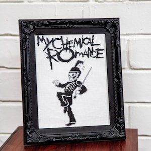 Op de afbeelding: Zwart-witte kruissteekborduursel van het logo van My Chemical Romance en een skeletfiguur in militair uniform. De borduursel is ingelijst in een zwart, versierd frame.