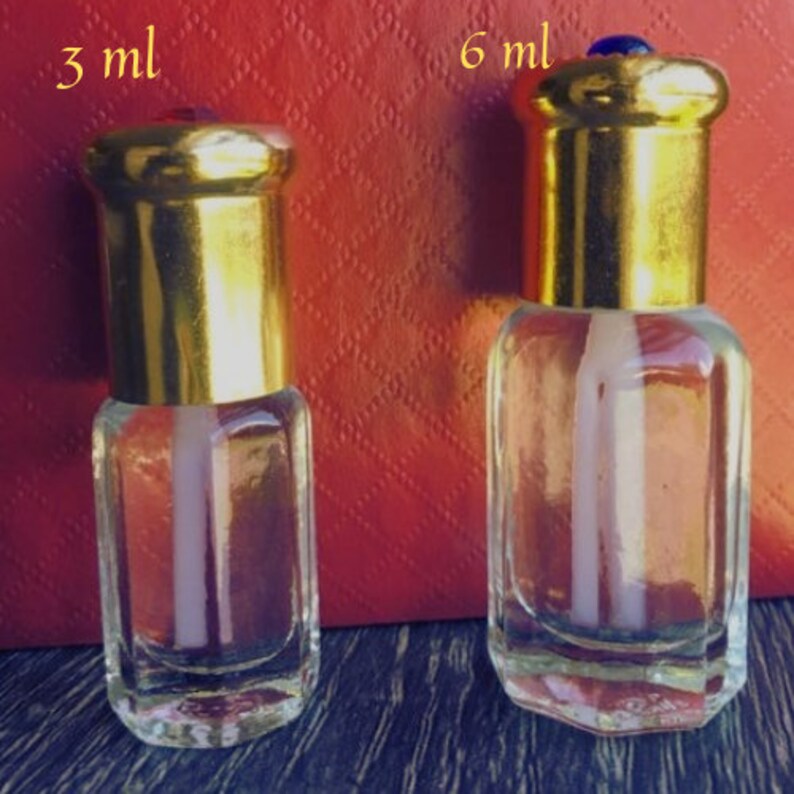 Puede incluir: Dos frascos de perfume de vidrio transparente con tapas doradas. Uno est&aacute; etiquetado "3 ml" y el otro "6 ml". Los frascos tienen forma rectangular con tapa dorada y cuerpo de vidrio transparente. El fondo es una superficie roja texturizada.