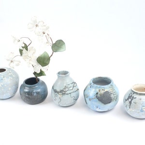 May include: Five ceramic vases in varying shades of blue and gray, arranged in a row. One vase holds white flowers. The vases have unique textures and patterns, with a speckled or marbled appearance. The vases are decorative.
