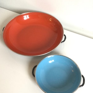 May include: Two enamel cookware pots with black handles. The larger pot is orange and the smaller pot is blue.