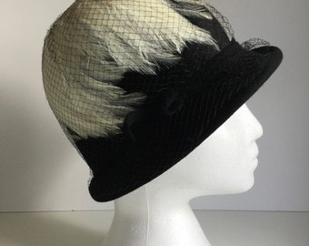 May include: A black felt hat with a white feather trim and a black net veil.