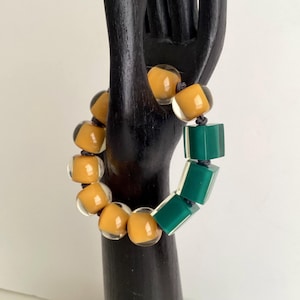 May include: A bracelet made of round, translucent amber-colored beads and square, translucent green beads. The beads are strung on a dark cord.