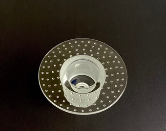 May include: A clear glass candle holder with a textured, dotted surface. The holder has a wide base and a smaller, cylindrical opening for the candle.