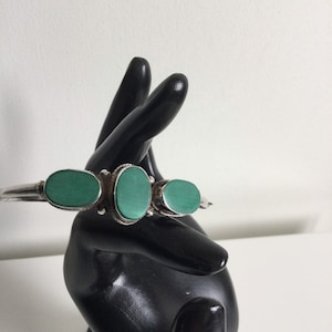 May include: A silver bracelet with three oval-shaped green stones.