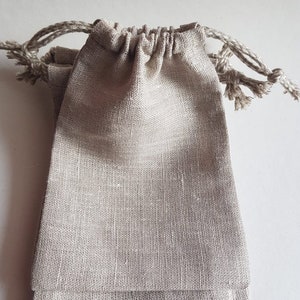 Puede incluir: Tres bolsas de yute natural con cordón de ajuste de color beige. Las bolsas están apiladas una encima de la otra.