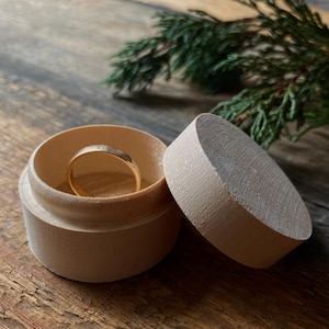 Puede incluir: Una caja de madera para anillos con tapa, la caja está abierta y hay un anillo de oro dentro.