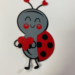 May include: A gray ladybug with red cheeks and a red heart in its hands. The ladybug has black spots on its red shell.