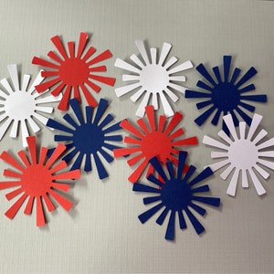 May include: A collection of red, white, and blue paper cutouts shaped like stars with rays. The cutouts are arranged in a cluster on a light gray background.