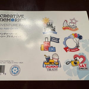 Puede incluir: Una hoja de pegatinas coloridas con temática de parque de atracciones. Las pegatinas incluyen imágenes de una montaña rusa, una noria, un castillo, una maleta, una cámara, un perrito caliente, palomitas de maíz y globos. El texto en las pegatinas incluye "Whee!", "Vacay Mode", "Big Smiles", "Yummy Treats!" y "Say Cheese!"