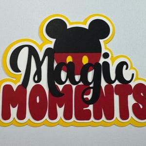 May include: A yellow, red, and black paper cutout of Mickey Mouse's head with the words "Magic Moments" in black lettering.