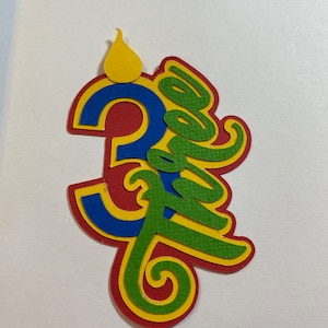 May include: A colorful paper cutout of the number "3" with a flame on top and the word "three" written in a decorative script. The number is red, blue, and yellow, and the word "three" is green, yellow, and red.