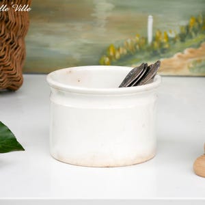 May include: A white ceramic mug with a black handle and the text "But First, Coffee" in a bold, black font. The mug is set against a blurred background, suggesting a cozy setting.