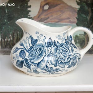 Peut inclure: Un pot à crème en céramique blanche avec un motif floral bleu et blanc. Le pot à crème présente un motif de roses bleues et blanches.
