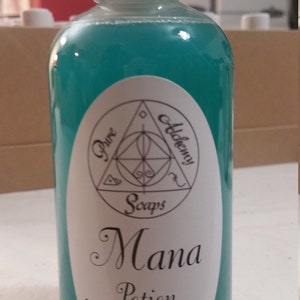 May include: A teal-colored liquid soap bottle with a white cap. The label reads "Pure Alchemy Soaps" and "Mana Potion Liquid Soap". The bottle is filled with a vibrant, turquoise liquid. The product is likely a cosmetic or personal care item.