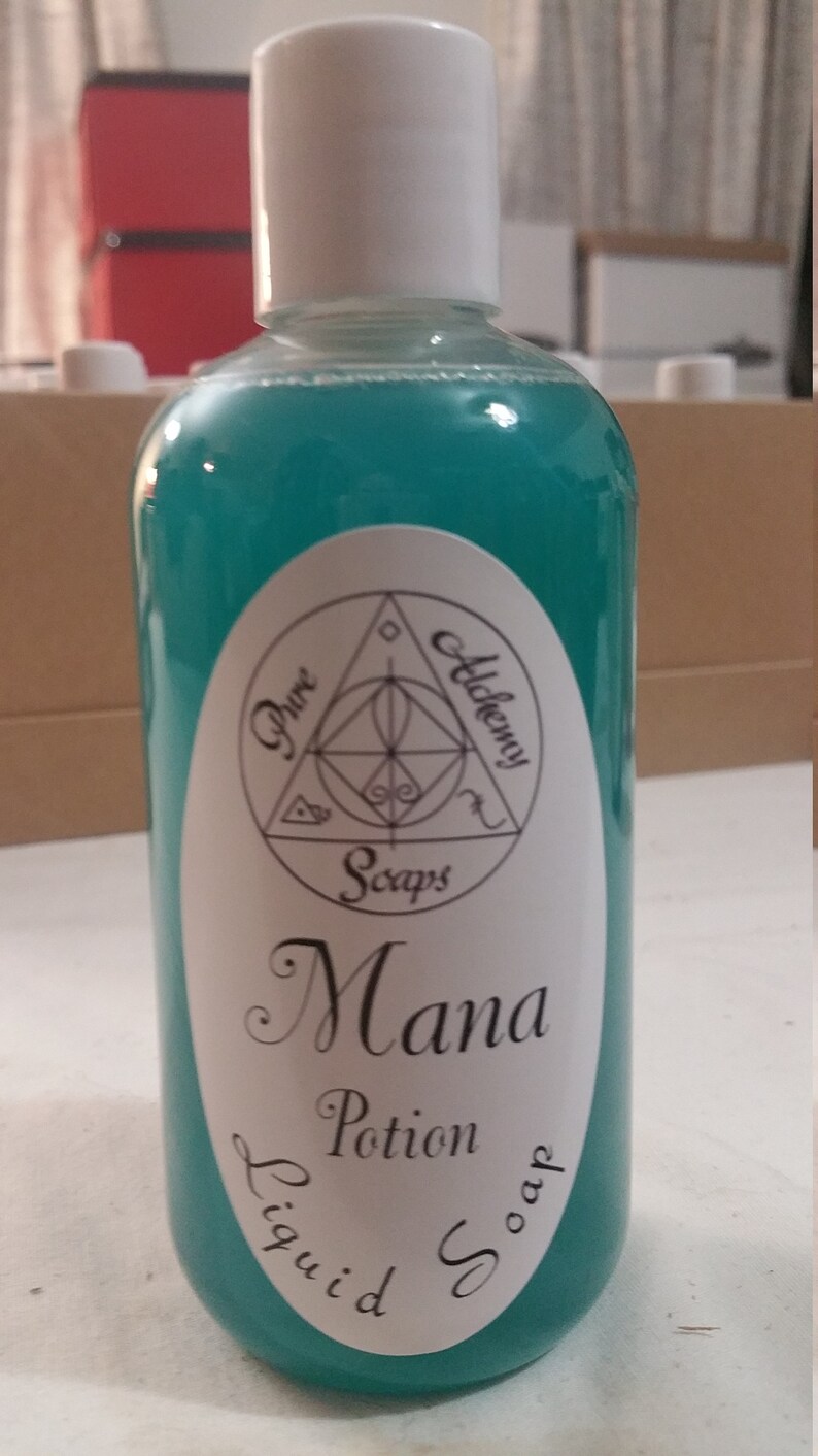 May include: A teal-colored liquid soap bottle with a white cap. The label reads "Pure Alchemy Soaps" and "Mana Potion Liquid Soap". The bottle is filled with a vibrant, turquoise liquid. The product is likely a cosmetic or personal care item.
