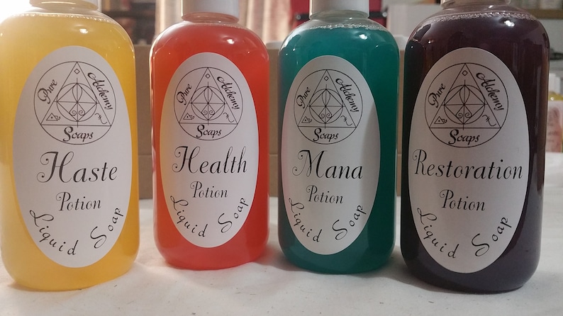 May include: Four bottles of liquid soap with white labels and the text "Pure Alchemy Soaps." The bottles contain yellow, red, teal, and purple liquids. The labels read "Haste Potion," "Health Potion," "Mana Potion," and "Restoration Potion."