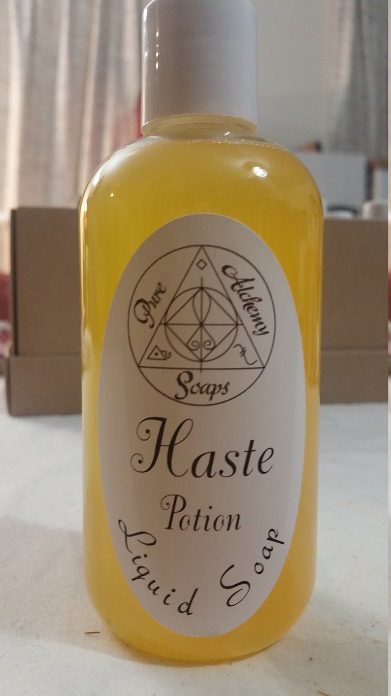 May include: A clear bottle of yellow liquid soap with a white cap. The label reads "Pure Alchemy Soaps" and "Haste Potion Liquid Soap" in elegant script. The bottle is approximately 8 inches tall.