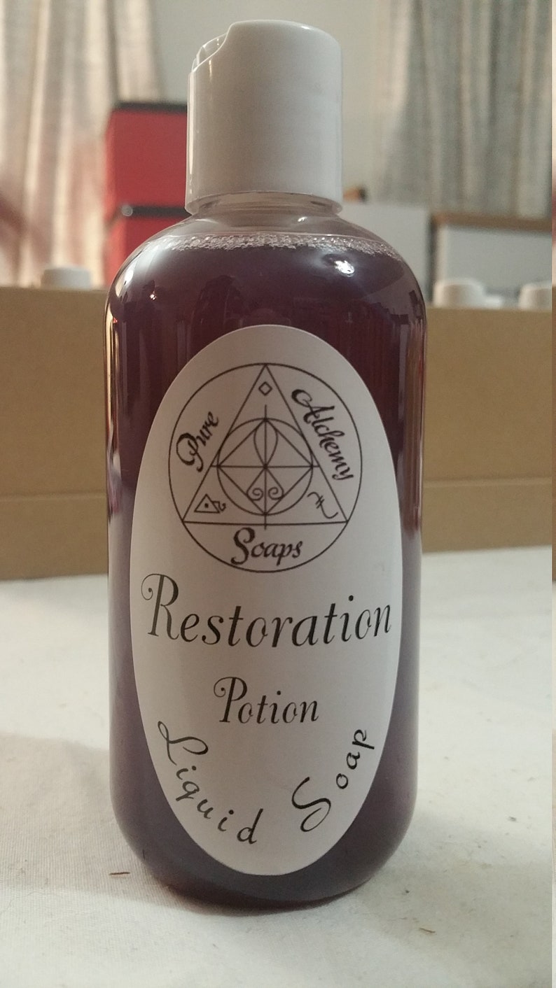 May include: A clear plastic bottle with a white cap, filled with a deep purple liquid soap. The label reads "Pure Alchemy Soaps" and "Restoration Potion Liquid Soap" in elegant script. The bottle is designed for liquid soap.