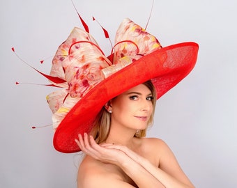 Può includere: Un grande cappello rosso a tesa larga con un motivo floreale. Il cappello è fatto di paglia e ha un grande fiocco in cima. Il cappello è indossato da una persona con i capelli lunghi e biondi.