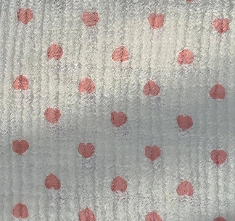 May include: White fabric with a pink heart pattern. The hearts are evenly spaced and are a light pink color.