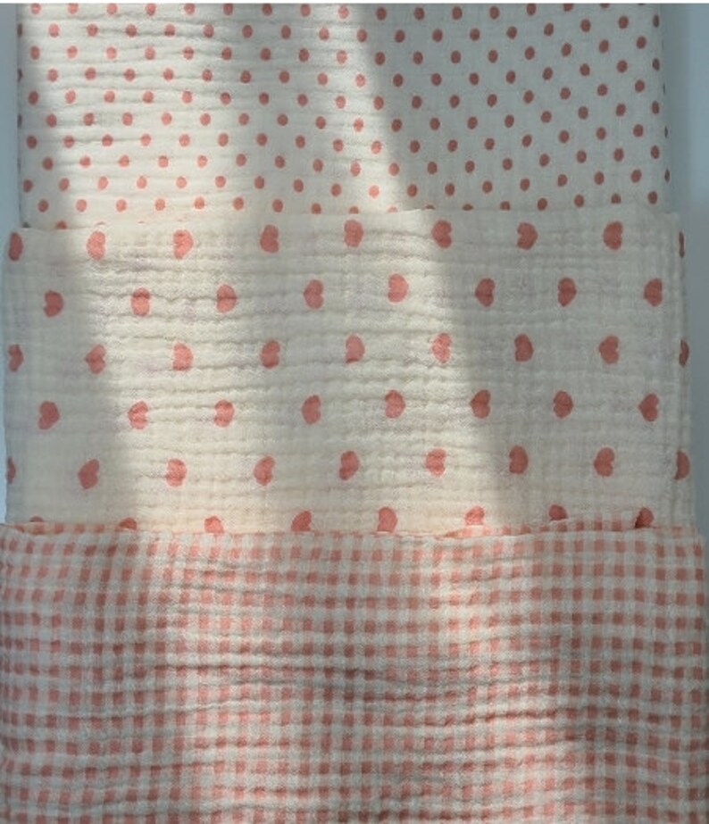 May include: Three pieces of fabric with different patterns. The top piece has small pink dots on a white background. The middle piece has small pink hearts on a white background. The bottom piece has a pink and white gingham pattern.