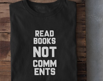 May include: Black t-shirt with white text that reads "Read Books Not Comments". The t-shirt is folded and laid on a wooden surface.