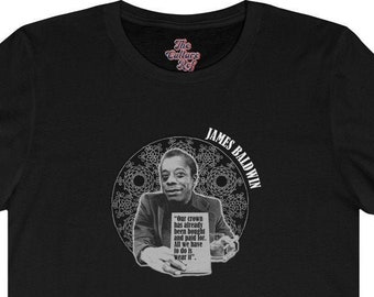Puede incluir: Camiseta negra con un gráfico blanco de James Baldwin sosteniendo un libro con la cita "The crown has already been placed, and paid for, and we have to wear it."