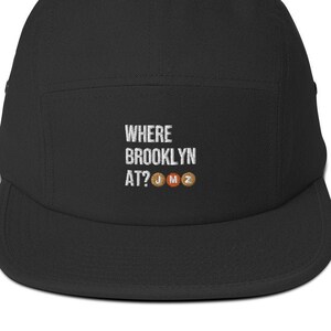 May include: Black 5-panel cap with white embroidered text that reads "WHERE BROOKLYN AT?" and three subway tokens with the letters J, M, and Z.