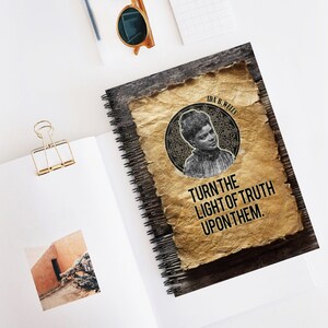 May include: A spiral bound notebook with a wood grain cover. The front cover features a vintage-style image of Ida B. Wells, a prominent African American journalist and activist. The image is surrounded by a decorative border and the text "TURN THE LIGHT OF TRUTH UPON THEM."