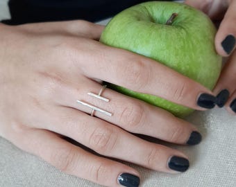 May include: A silver ring with a simple geometric design. The ring is worn on a finger holding a green apple.
