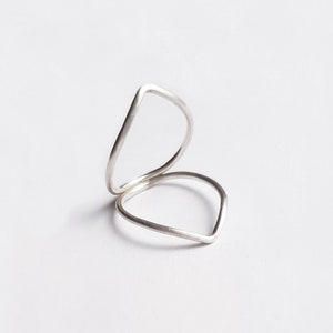 Puede incluir: Dos anillos de plata, uno apilado sobre el otro, ambos con forma de lágrima.