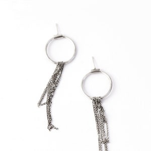 Peut inclure: Une paire de boucles d'oreilles argentées. Chaque boucle d'oreille est composée d'un cercle avec plusieurs brins de chaînes délicates qui tombent vers le bas. Les boucles d'oreilles sont posées sur un fond blanc, soulignant leur design minimaliste.
