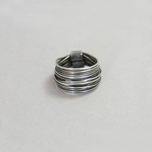 May include: A silver ring with multiple bands of wire wrapped around each other. The ring is thick and has a rounded shape.