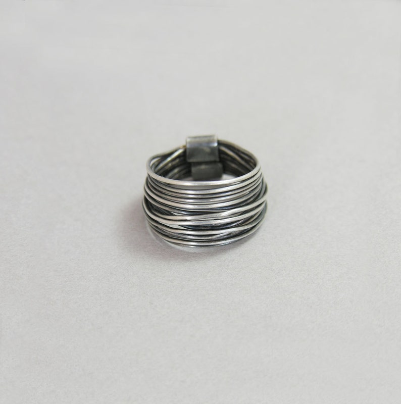 May include: A silver ring with multiple bands of wire wrapped around each other. The ring is thick and has a rounded shape.