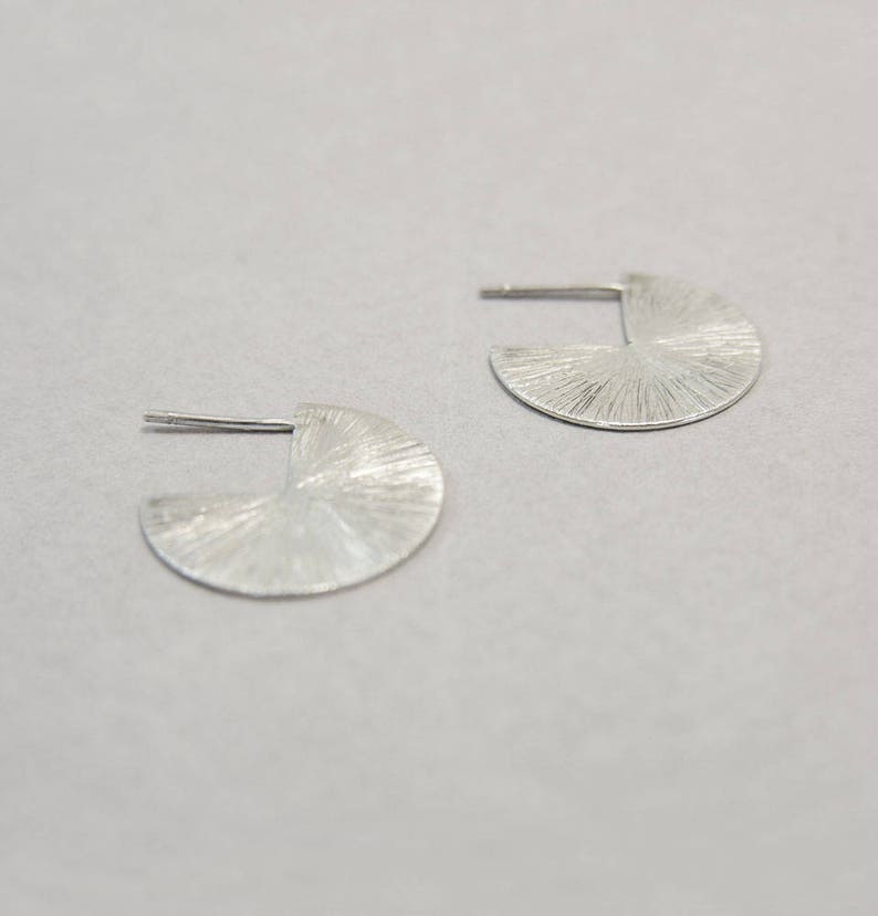 May include: A pair of silver earrings with a textured, circular design. The earrings are made of a smooth, shiny metal.
