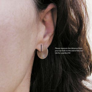 May include: A close-up of a person's ear wearing a silver half-circle earring with a textured surface. The text "Please measure the distance from your ear hole to the end of the ear lob for a perfect fit!" is visible below the earring.