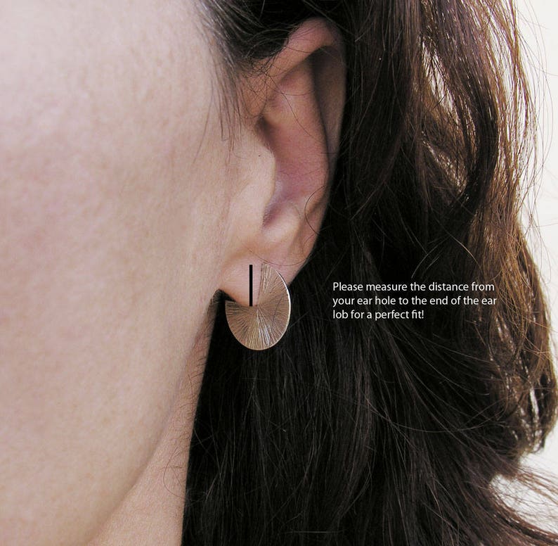 May include: A close-up of a person's ear wearing a silver half-circle earring with a textured surface. The text "Please measure the distance from your ear hole to the end of the ear lob for a perfect fit!" is visible below the earring.