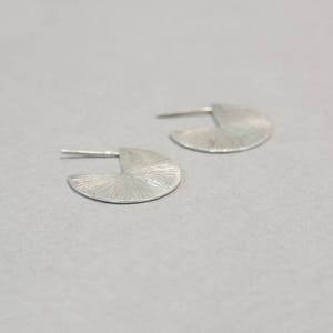 May include: A pair of silver earrings with a textured, fan-shaped design.