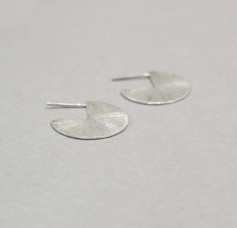 May include: A pair of silver earrings with a textured, fan-shaped design.