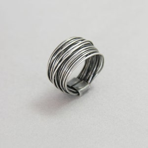 May include: A silver ring made of multiple thin wires woven together. The ring is wide and has a rounded shape.