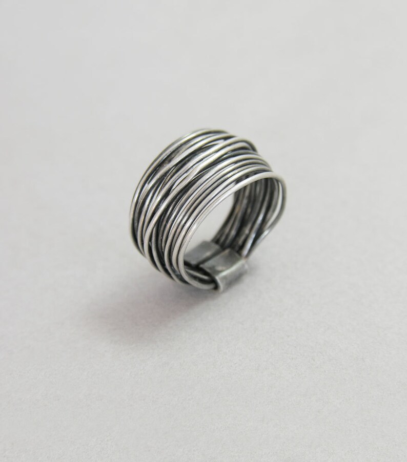 May include: A silver ring made of multiple thin wires woven together. The ring is wide and has a rounded shape.