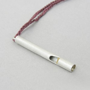 May include: A silver whistle pendant with a gold accent on a maroon cord.
